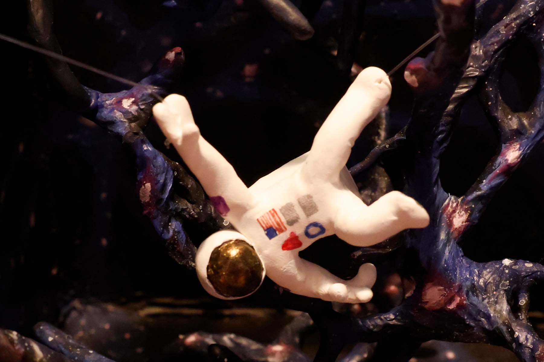 An extreme closeup of the astronaut near the spider. An American flag, a red triangle, and a blue circle are visible on the chest pack of their space suit.