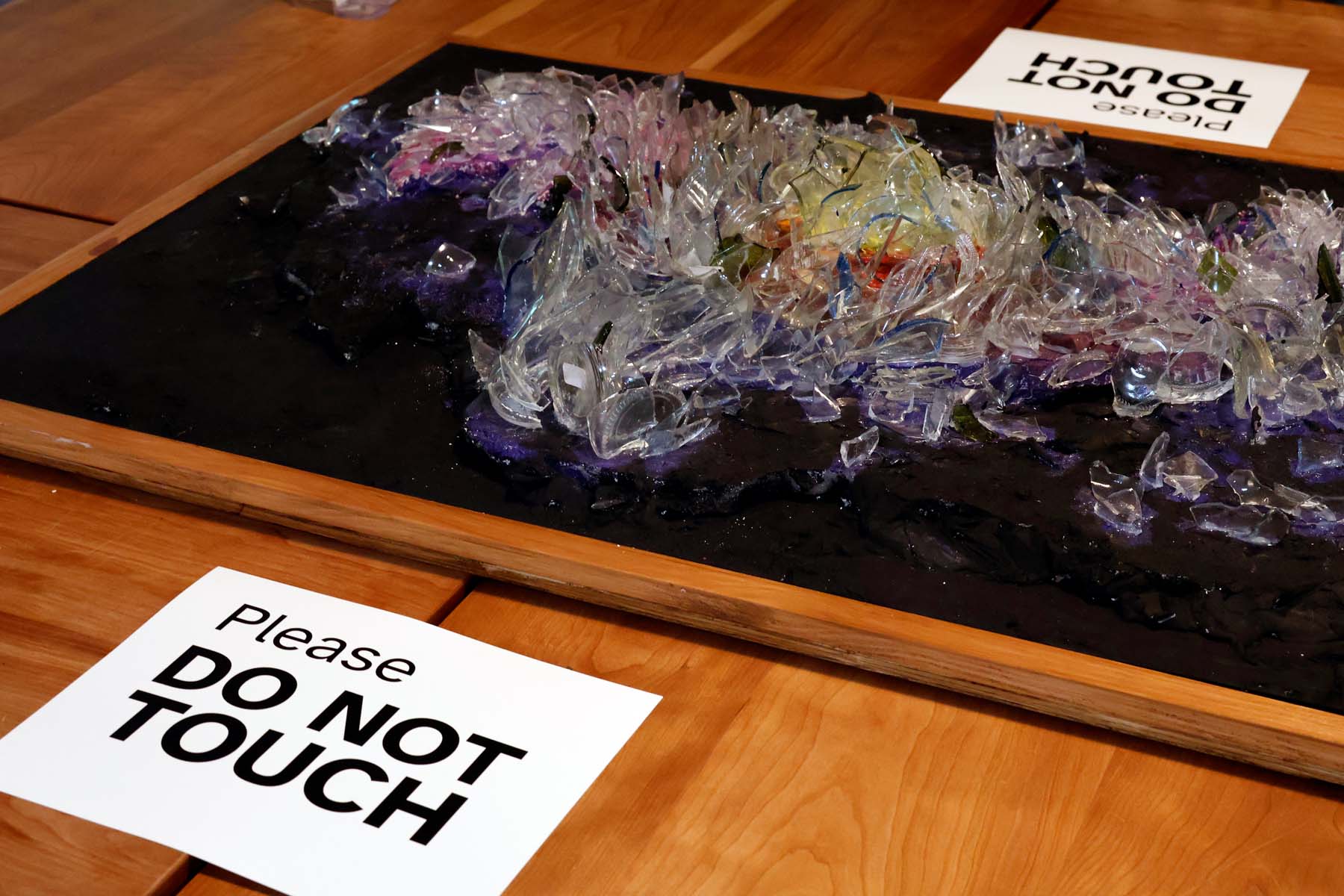 Glass galaxy relief sculpture from slightly above, sitting on a wooden table with a label "Please DO NOT TOUCH".